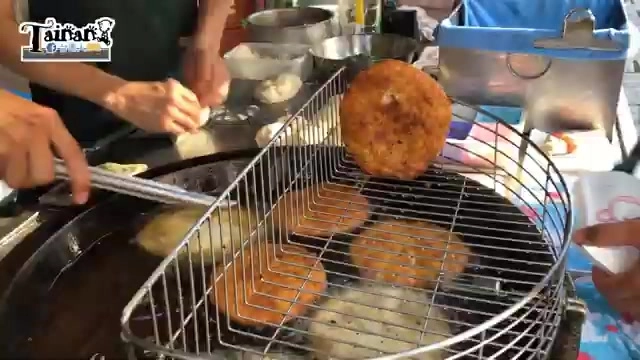 店家在鐵板上煎製多個燒餅，金黃酥脆的成品堆疊在鐵網架上