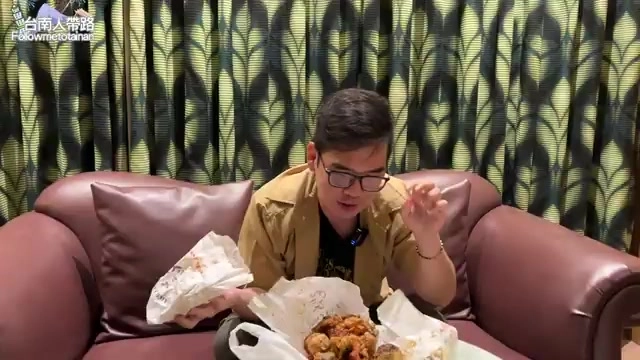 阿波坐在沙發上享用外帶鹹酥雞,手上拿著醬燒雞排大快朵頤