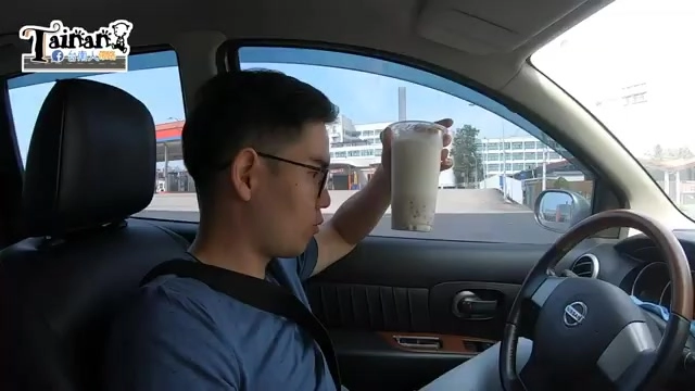 男子在車內舉起飲料杯準備飲用,杯中可見上層乳白色與下層顆粒分明的配料