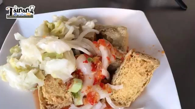 白色瓷盤盛著炸臭豆腐，鋪滿高麗菜絲、生洋蔥與紅色辣椒醬汁