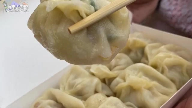 筷子夾起的小籠包,皮薄透亮,內餡隱約可見,盒中排列著多顆小籠包