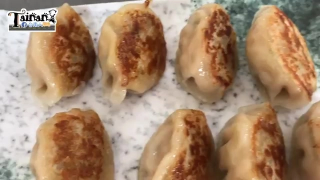 白色石板盤上排列著多顆煎餃,底部呈現金黃焦香色澤,摺邊細緻