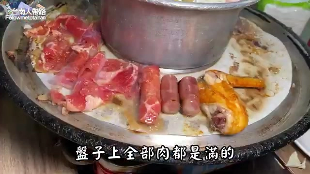 鐵盤上盛滿生鮮肉品，包含大塊豬肉、香腸與雞腿肉，份量豐盛