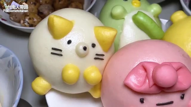 多顆造型可愛的貓爪包排列在盤中，包含黃色貓咪造型、綠色與粉色動物造型的包子