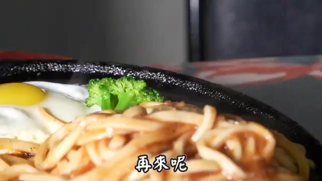 黑色鐵板上盛著粗麵條，搭配煎蛋與花椰菜，醬汁濃郁裹滿麵條