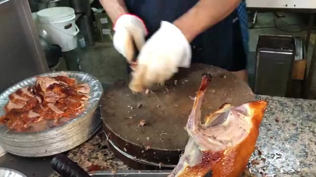 師傅戴著手套正在砧板上片切烤鴨，一旁托盤已擺放切好的鴨肉片