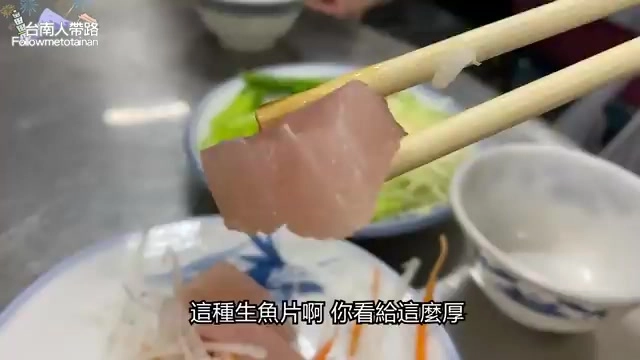 筷子夾起厚切的生魚片,肉質粉紅細嫩,旁邊擺著蘿蔔絲配菜