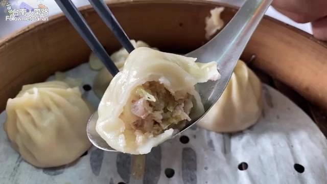 筷子與湯匙夾起半顆湯包,內餡帶著蔥花,湯汁清晰可見