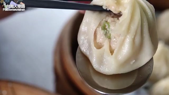 湯包立在湯匙上,皮薄透亮,內餡與蔥花隱約可見,湯汁飽滿