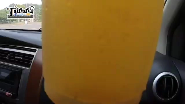 車內特寫金黃色楊桃汁裝在透明杯中，杯身標籤可見店家字樣
