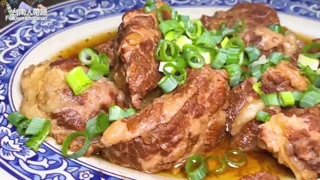 盤中盛著醬色油亮的紅燒牛肉塊，撒上翠綠蔥花點綴