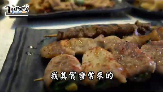 黑色石板盤上擺著多支肉串與圓形肉塊串燒，表面撒上紅色辣椒粉，油亮誘人