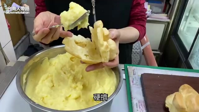 老闆娘正用湯匙將濃郁的黃色卡士達醬填塞進泡芙中,餡料滿溢