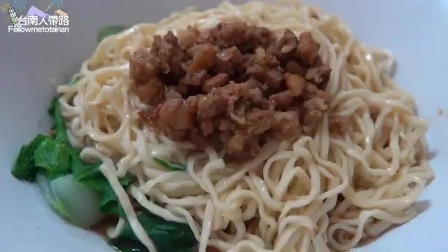 白色瓷碗盛著乾拌意麵，鋪上深色肉燥，搭配燙青江菜