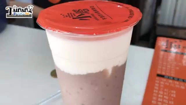 透明塑膠杯裝著芋頭西米露，上層白色奶蓋與下層紫褐色芋頭西米露分層明顯，杯蓋印有店家紅色圓形標誌