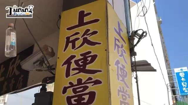 黃底招牌上以紅字寫著「上欣便當」,直式招牌矗立在店門口