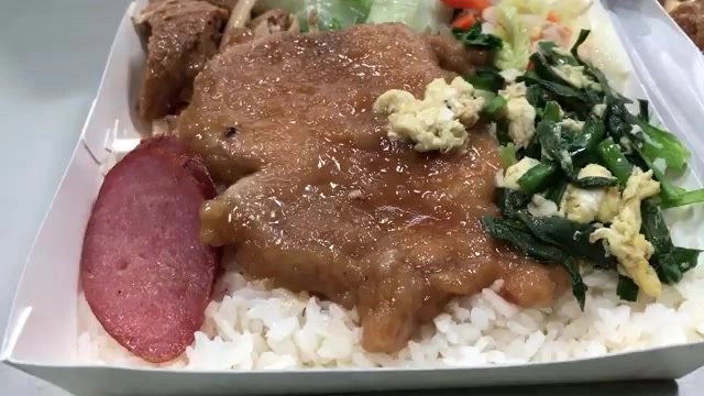 便當盒中盛著厚切滷排骨鋪在白飯上,搭配燙青菜、紅腸與炒蛋配菜
