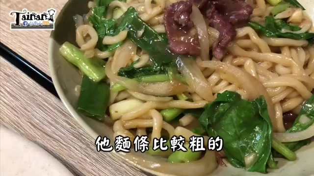 炒粗麵盛裝在白色瓷碗中,麵條裹著醬色,搭配牛肉片與燙青菜