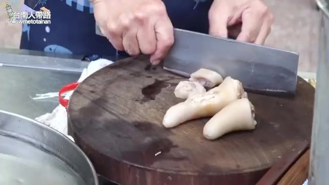 店家師傅在砧板上俐落切開新鮮豬尾巴，準備搭配蒜末醬油膏上桌