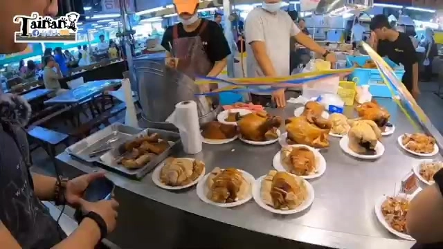 料理台上擺滿切盤的鹹水雞與甘蔗雞，色澤油亮，攤販正在忙碌服務排隊人潮