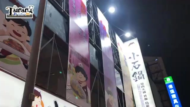 夜間店面外觀,燈箱招牌寫著「小石鍋」,門口懸掛多面宣傳布條