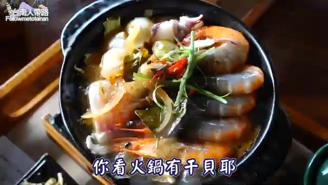 石鍋裡盛著蝦子、干貝與蔬菜的海鮮鍋,湯汁鮮紅誘人,蔥花點綴其上