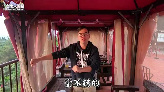 戶外紅色遮陽帳篷座位區,主持人站在其中介紹景觀餐廳周邊環境,遠方可見仁義潭湖景