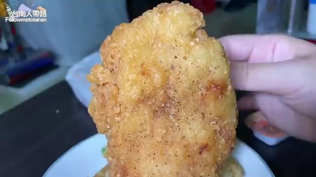 酥脆金黃色的雞排特寫,表面撒著胡椒粉,手指捏著一角
