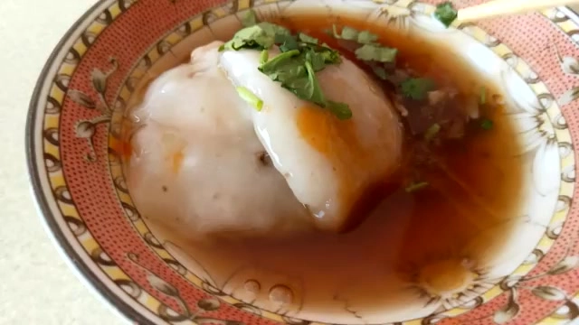 瓷碗中盛著菜粽，淋上醬油膏並撒上香菜與蒜蓉，湯汁油亮