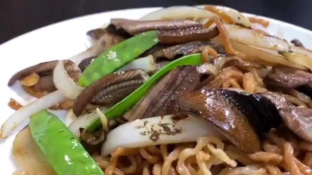 盤中鱔魚意麵鋪滿豆芽、洋蔥與荷蘭豆，鱔魚片色澤油亮