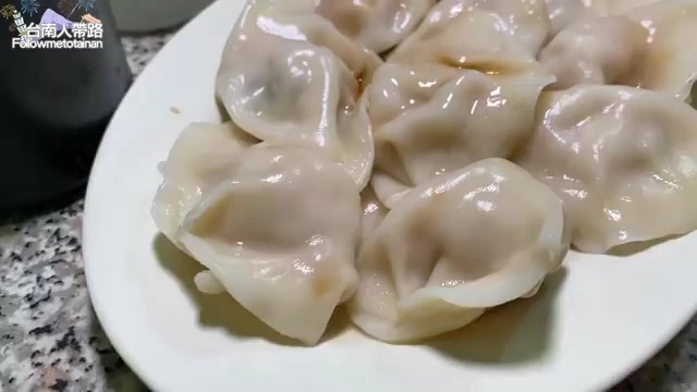 白色瓷盤中盛著多顆剛煮好的水餃，表面油亮，皮薄透光