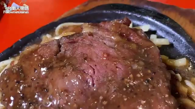 鐵盤上的牛排淋著濃郁醬汁,搭配麵條,色澤誘人