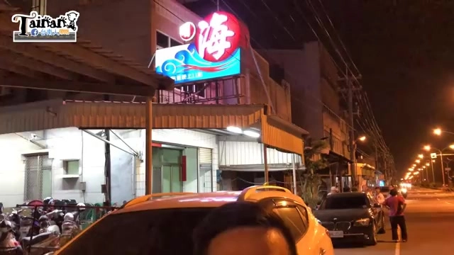 夜晚拍攝的店面外觀，紅底藍浪圖案招牌上寫著「海」字，遮陽棚下停放多台機車與汽車