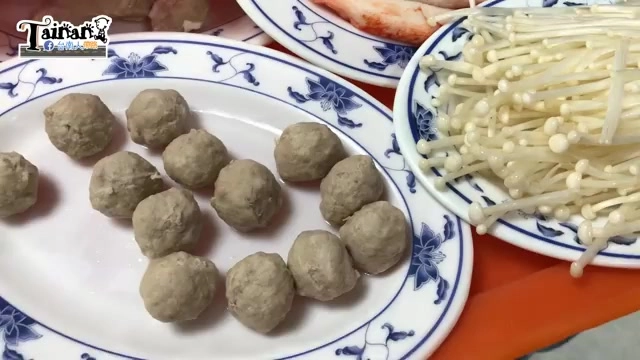白色瓷盤盛著多顆貢丸，旁邊搭配金針菇與其他火鍋料，色澤呈現淡褐色