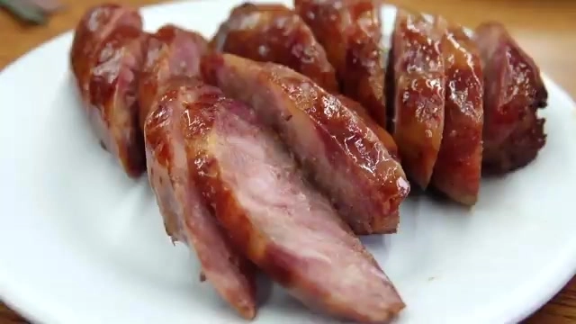 切片香腸色澤油亮紅潤,切面可見粉紅色肉質,盛裝在白色盤中