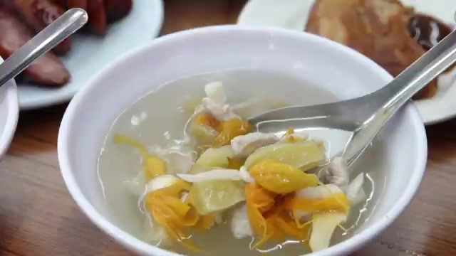 湯碗裡盛著清澈的湯品,可見薑黃色配料與肉絲,湯匙攪拌其中