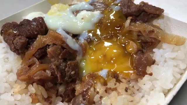 白色餐盒盛著牛肉飯，淋上溫泉蛋，蛋黃流淌在肉片與洋蔥之間