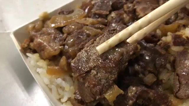 筷子夾起深色滷汁包覆的牛肉片，鋪在白米飯上，油亮誘人