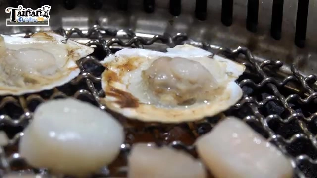 燒烤網上正在炙烤數顆帶殼干貝，湯汁在殼中滋滋作響，色澤晶瑩剔透
