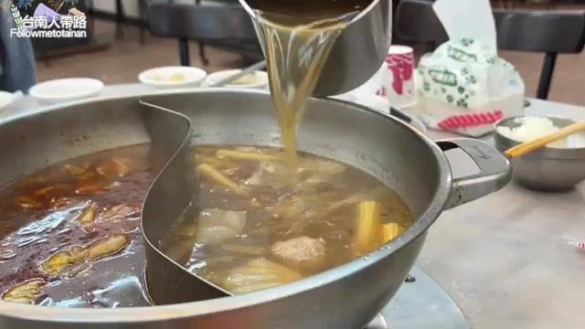 店員將湯頭倒入石頭鍋中，鍋內蔬菜配料滿滿，甘甜湯頭是店家招牌特色