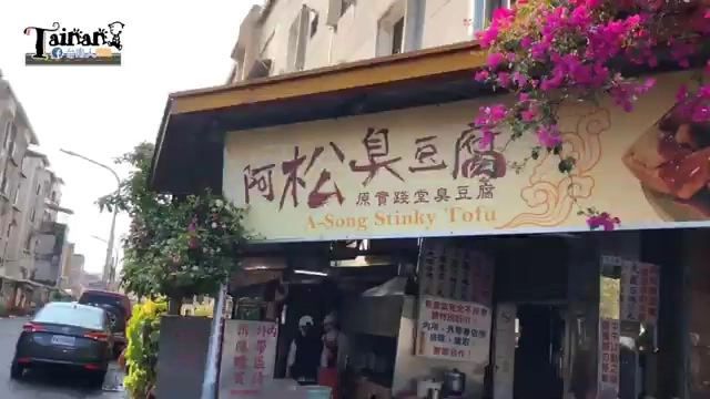 黃底招牌上寫著「阿松臭豆腐」與英文「A-Song Stinky Tofu」,搭配店家自產自銷字樣,門口花朵盛開