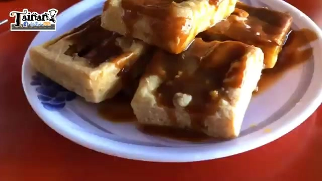 白色瓷盤盛著切塊酥炸臭豆腐,淋上深色特調醬汁,豆腐外皮呈現金黃色澤