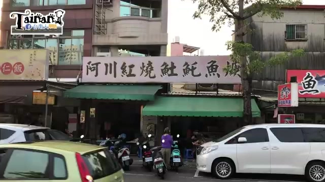 店面招牌，白底紅字寫著「阿川紅燒土魠魚焿」，綠色遮陽棚下停放機車，街道車水馬龍