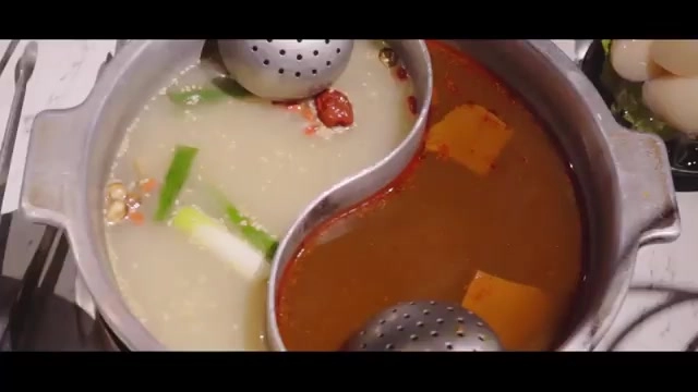 鴛鴦鍋底特寫，一側清湯搭配蔥段與紅棗，另一側紅湯帶著辣椒與胡蘿蔔，湯色分明