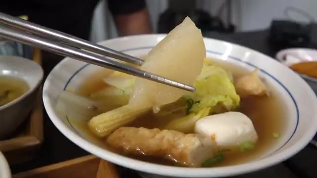 夾起一塊白蘿蔔的關東煮湯碗，湯色清澈，配料豐富包含豆腐與油豆腐