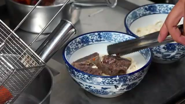 店員將燙好的牛肉與麵條盛入青花瓷碗中,準備淋上湯頭