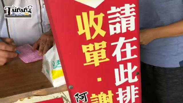 紅底黃字的排隊指示牌立在櫃檯前，寫著「請在此排收單」，一旁是點餐窗口與顧客身影