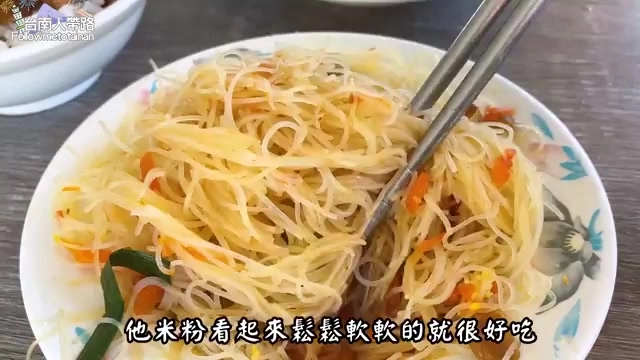 白色瓷盤中盛著淋上滷汁的炒米粉，夾雜著紅蘿蔔絲，筷子正夾起一撮