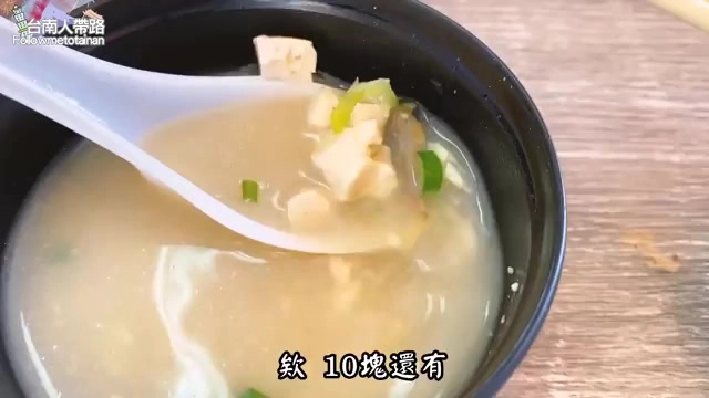 黑色碗中盛著味噌湯，內有豆腐塊與蔥花，湯匙舀起一口