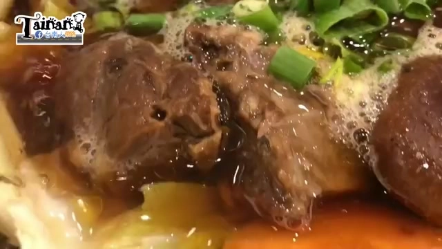 深色湯汁中的牛腩塊特寫，表面浮著油花與蔥花，湯汁滾動冒著細泡
